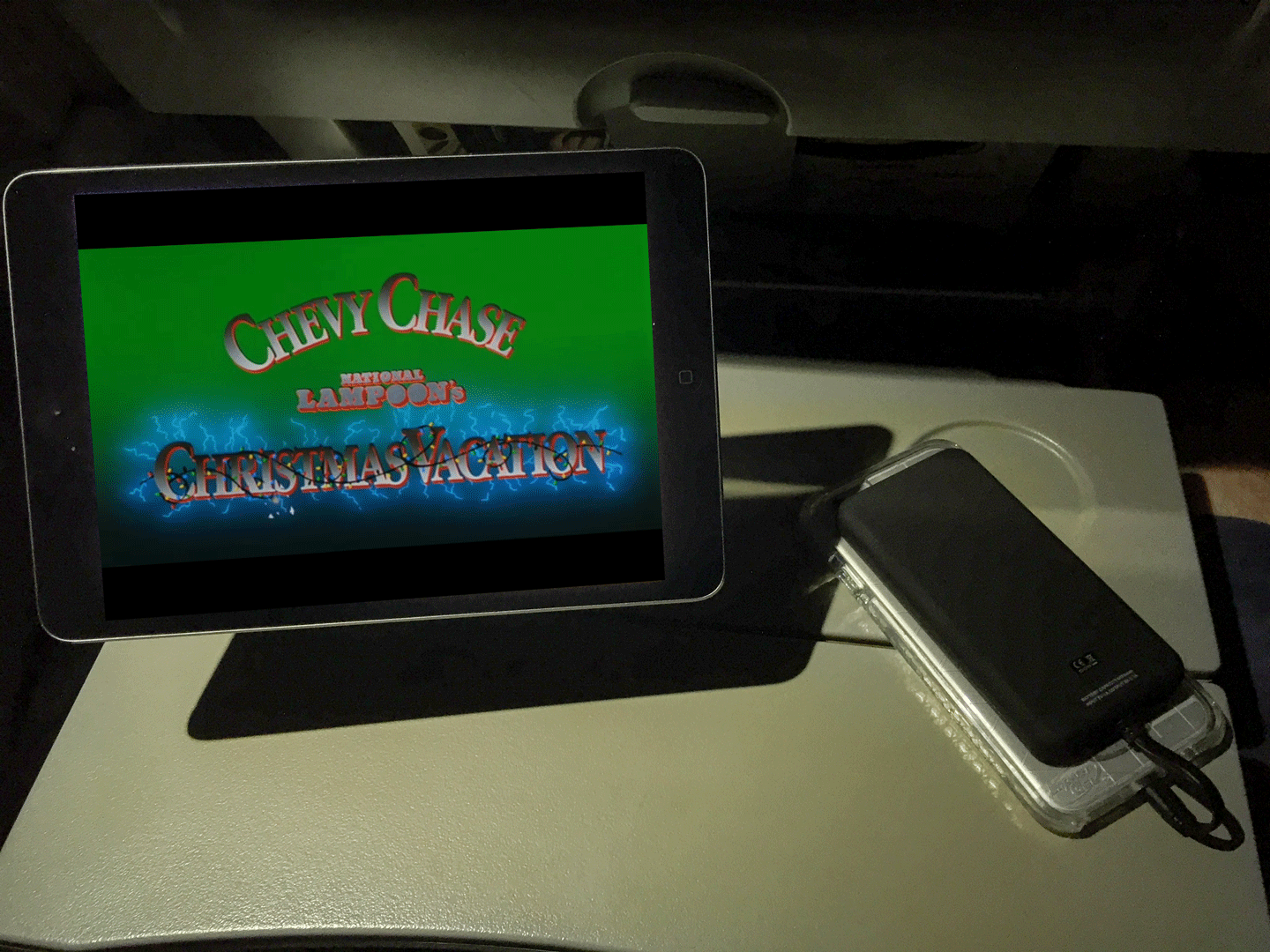 phone charging via portable power bank next to ipad playing National Lampoon's Chrismas vacation movie