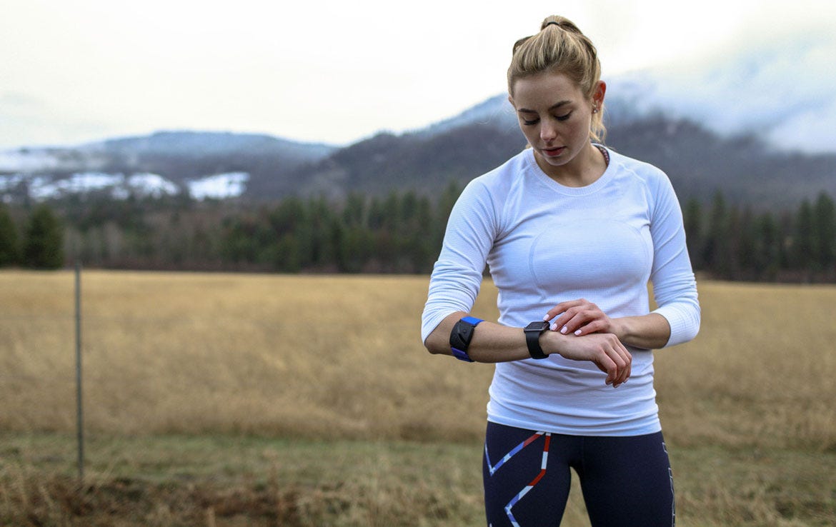 woman standing in field looking at watch while wearing Scosche armband heart rate montior