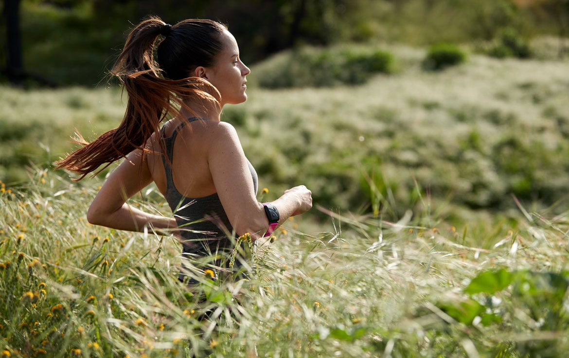 woman running through field with high grass wearing armband heart rate monitor