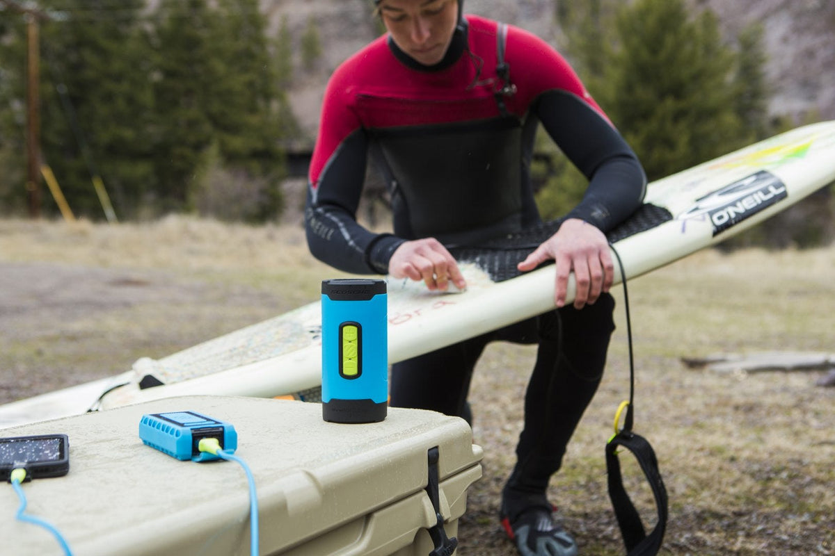 man with surf board charging phone via power bank and using wireless bluetooth speaker