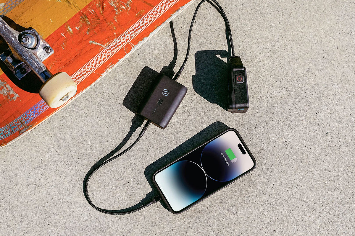 iphone and camera charging via scosche charging cable via Scosche portable power bank sitting on concrete floor next to skateboard