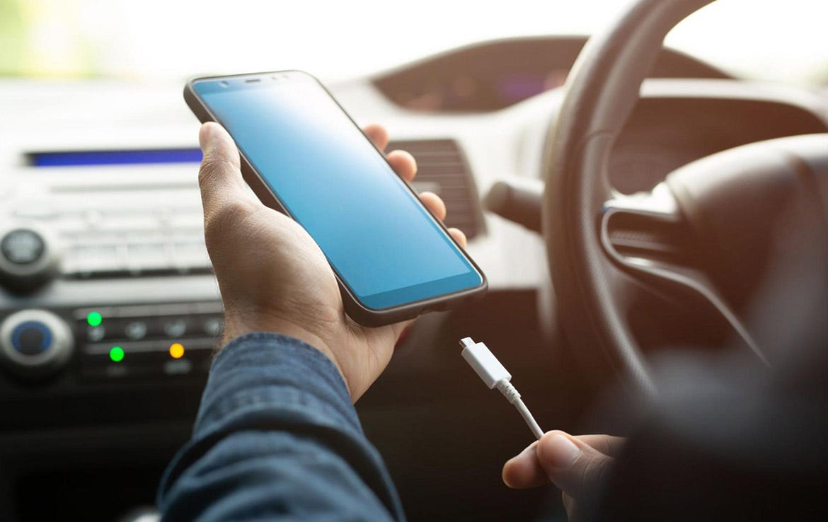 man holding phone and charging cable while sitting in car