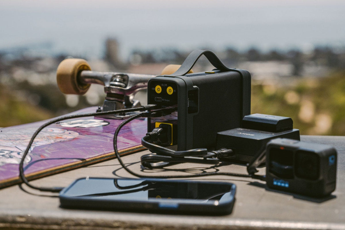 Portable power station charging phone camera and battery sitting on table next to skate board