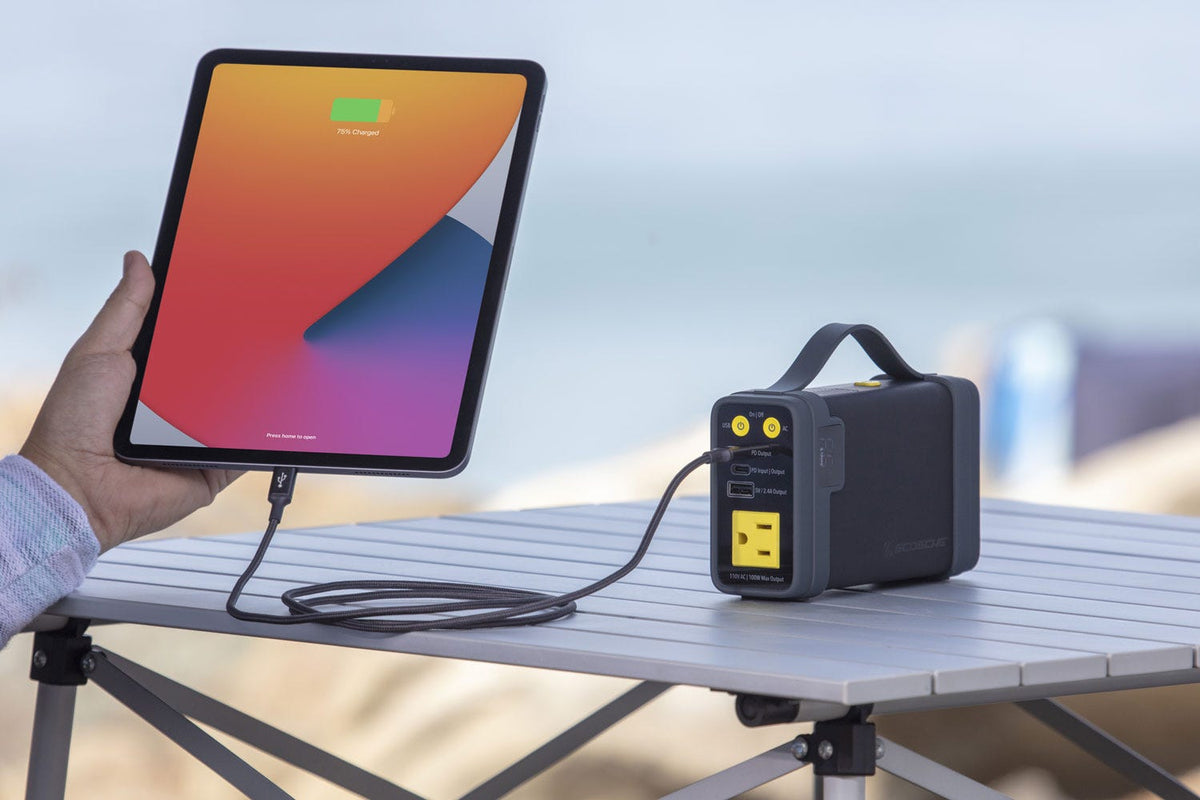 Man holding ipad charging via Scosche portable power station on table at the beach