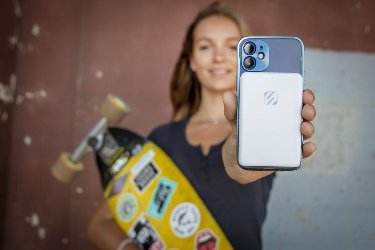 Woman holding skateboard and iphone with Scosche power bank attached to back of phone