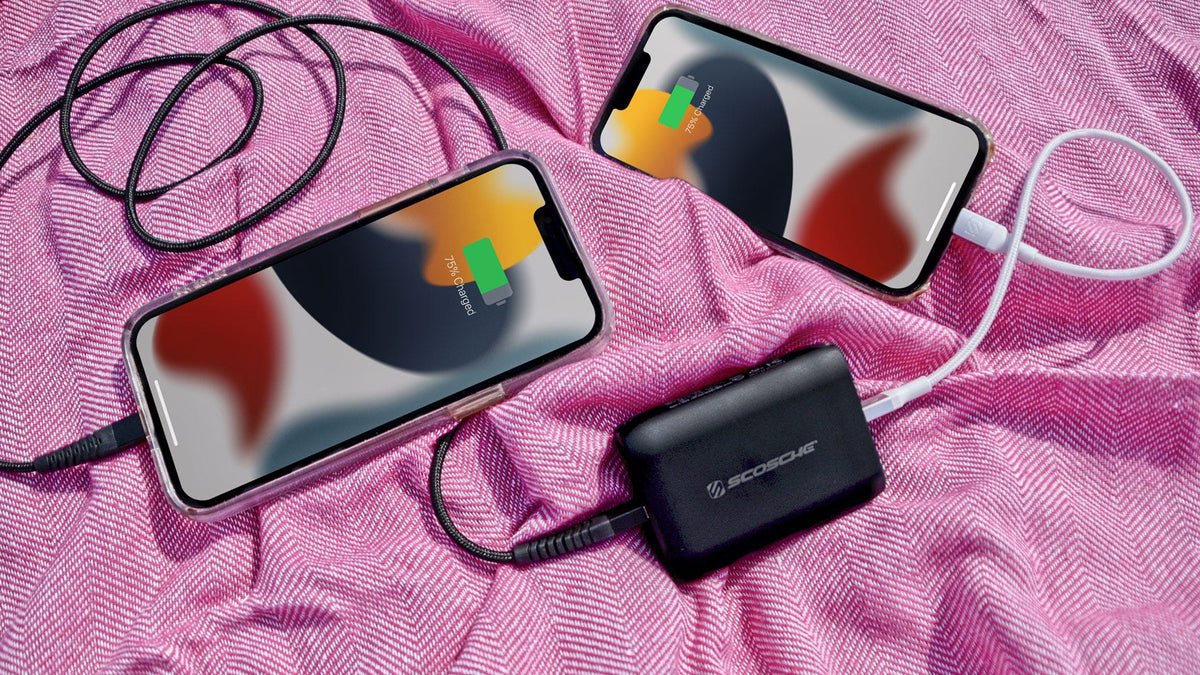 two iphones charging via Scosche portable power bank on pink fabric background