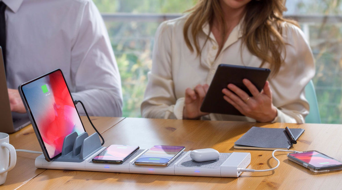 ipad, 2 iphones and Airpods charging via Scosche modular wireless charging pad with iphone charging via cable while sitting on office desk at meeting