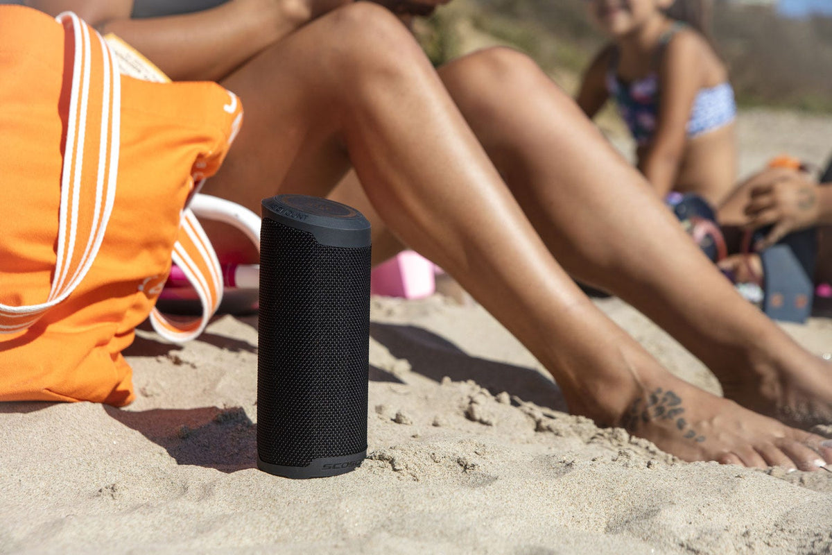 wireless bluetooth speaker on beach next to woman's legs