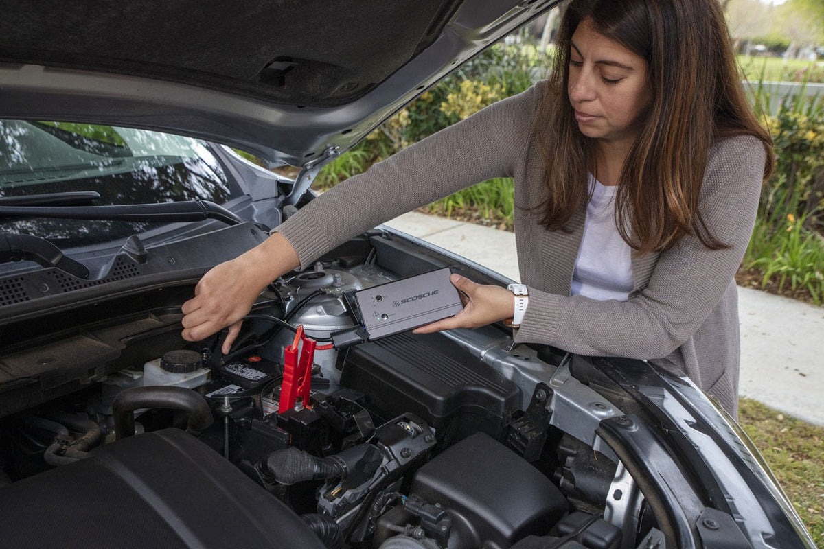 woman clamping portable jump starter on car battery