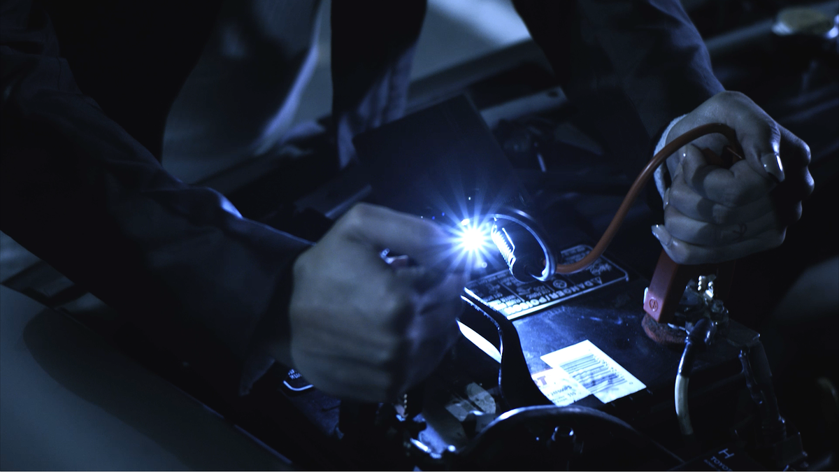 woman attaching portable jumper cables to car battery at night