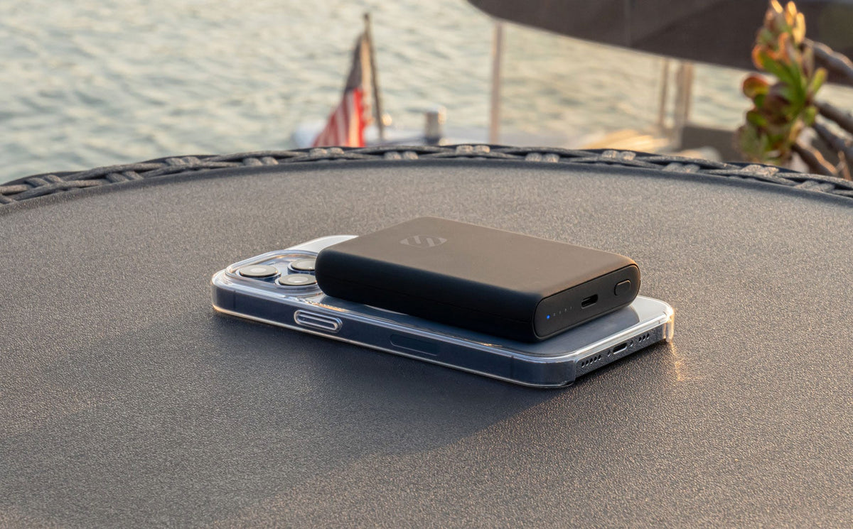 iphone with power bank charging on back while sitting on table next to lake