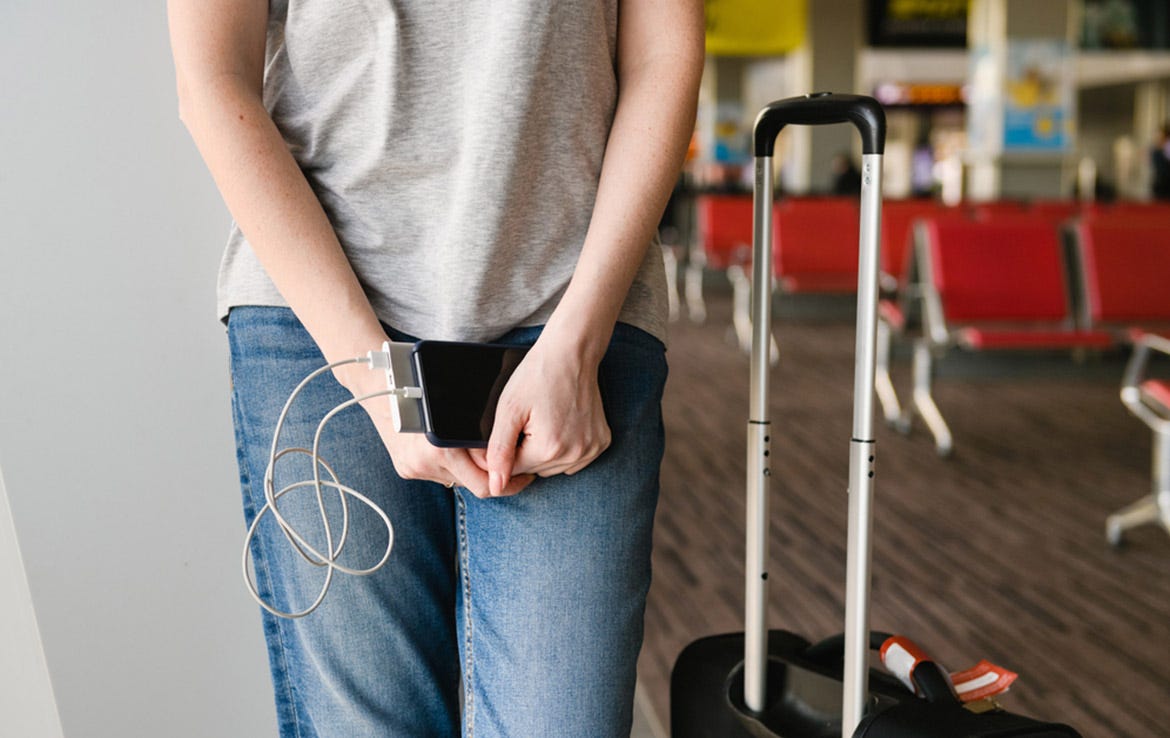 woman holding phone and power bank while standing next to luggage