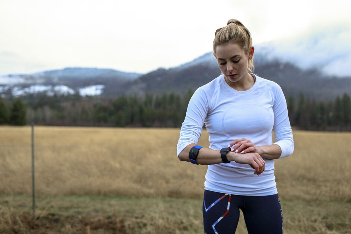 Woman standing in field looking at smart watch with armband heart rate monitor on arm