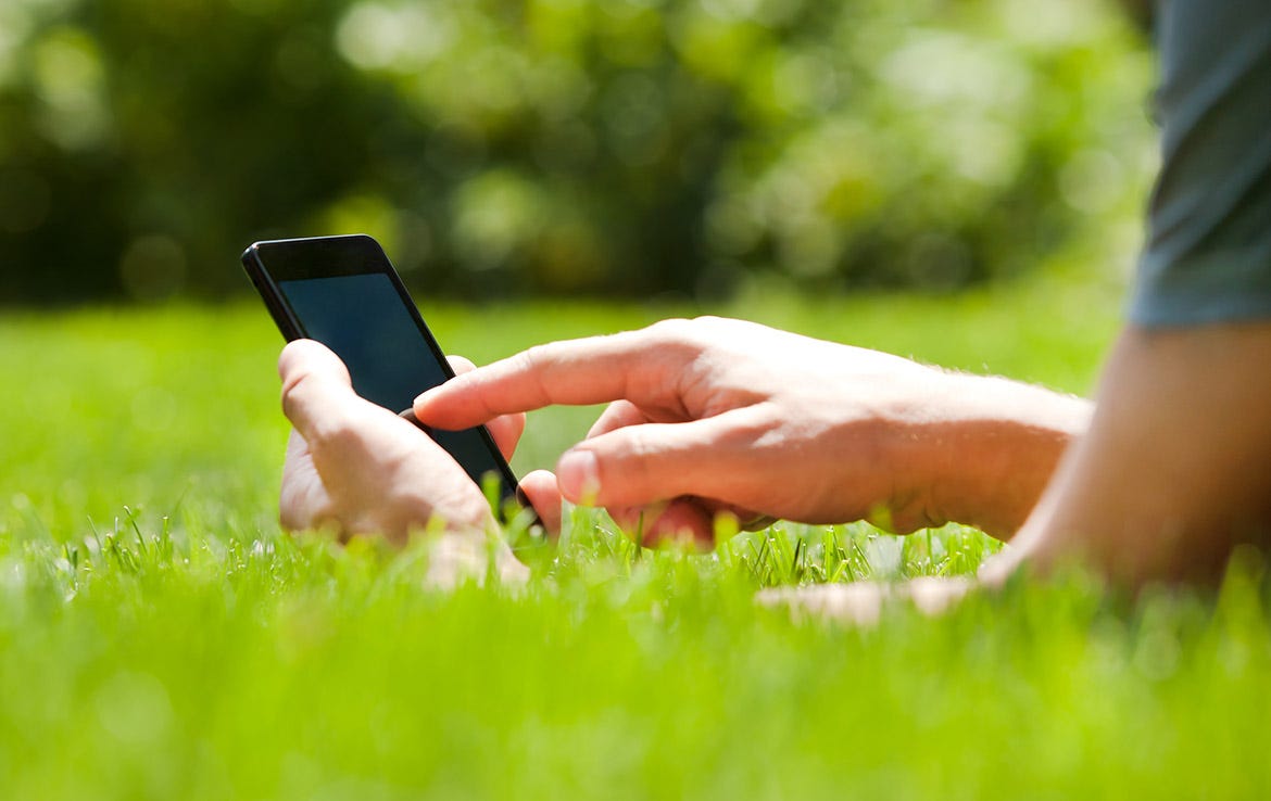 man laying in grass touching phone screen