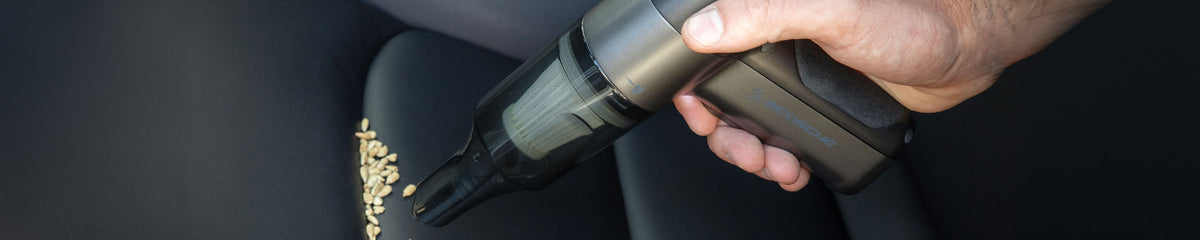 Hand holding small vacuum on car seat getting crumbs