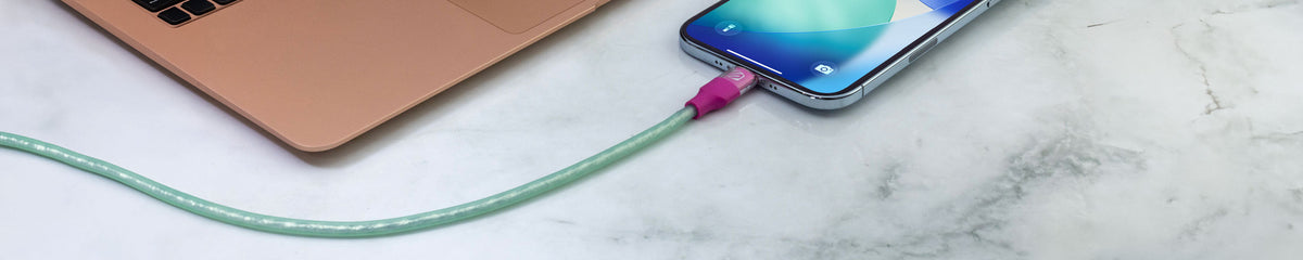 iPhone with a purple and green cable plugged into it next to a gold laptop