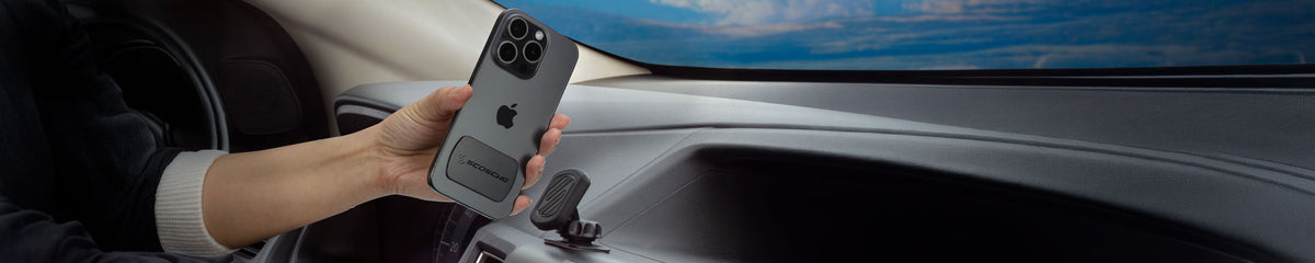 Hand holding iPhone with metalic plate on it up to magnetic phone mount on vehicle dashboard