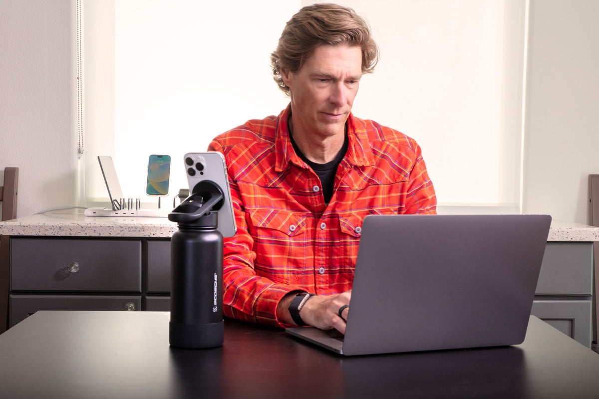 Man working on laptop with water bottle next to him with phone attached