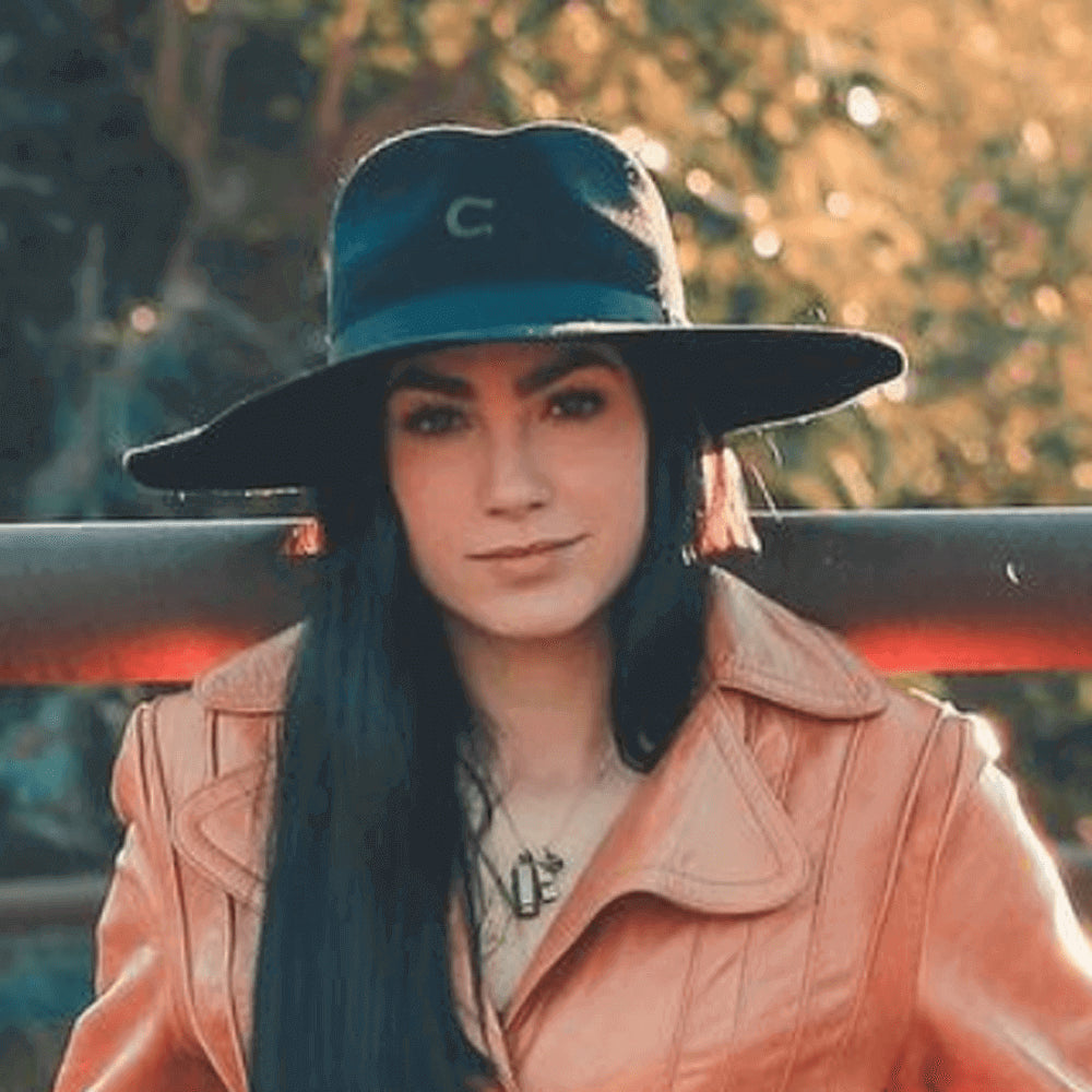 Pfieffer poses in front of a metal pipe and is wearing a black hat and a pink leather jacket.