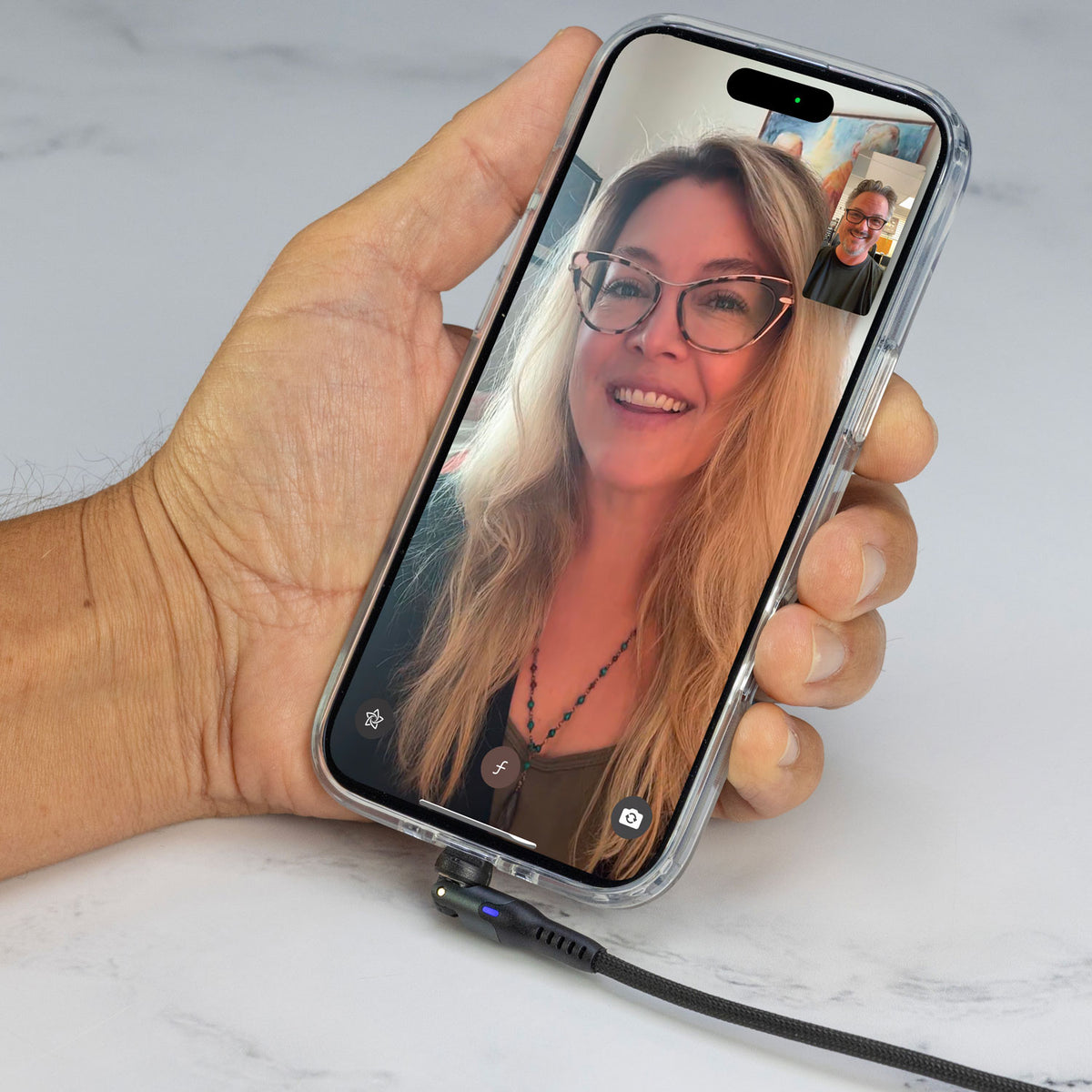 Hand holding phone with FaceTime with woman on screen and a cable plugged into it the bottom of the phone