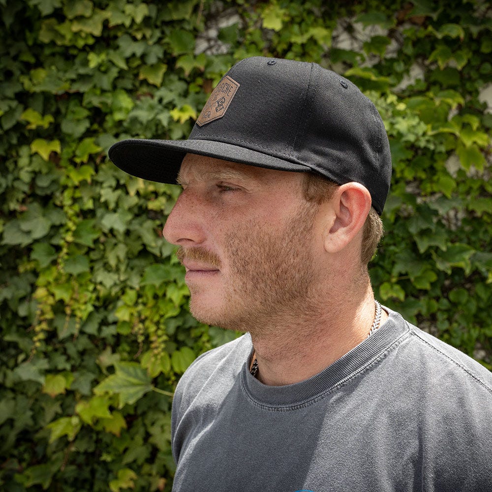 side view man wearing black hat with bush in background
