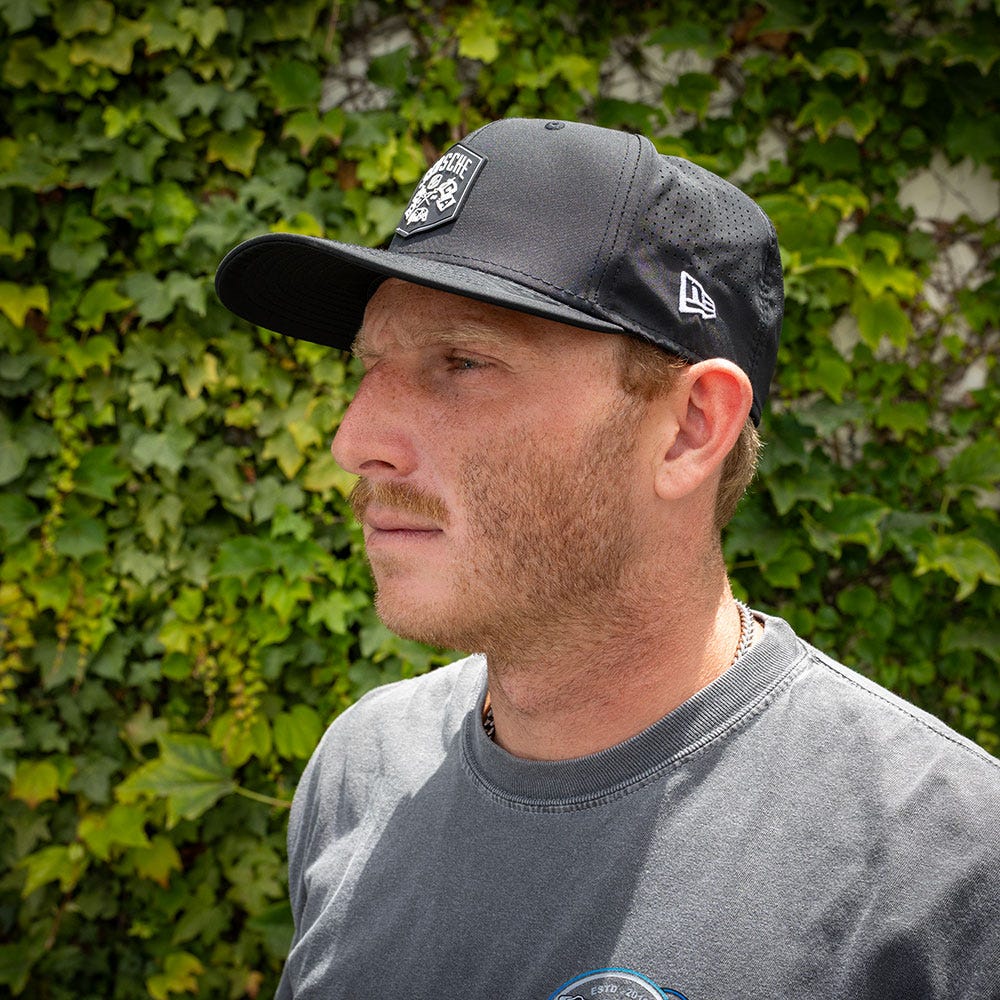 side view man wearing black hat with bush in background