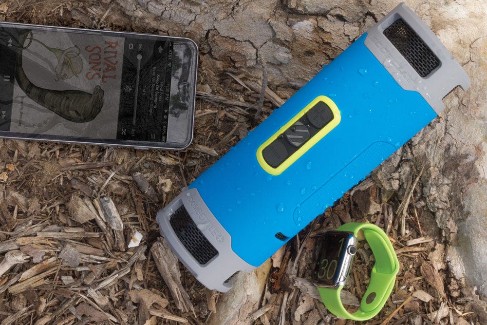 boombottle portable speaker next to apple watch and iphone playing music app while laying on mulch