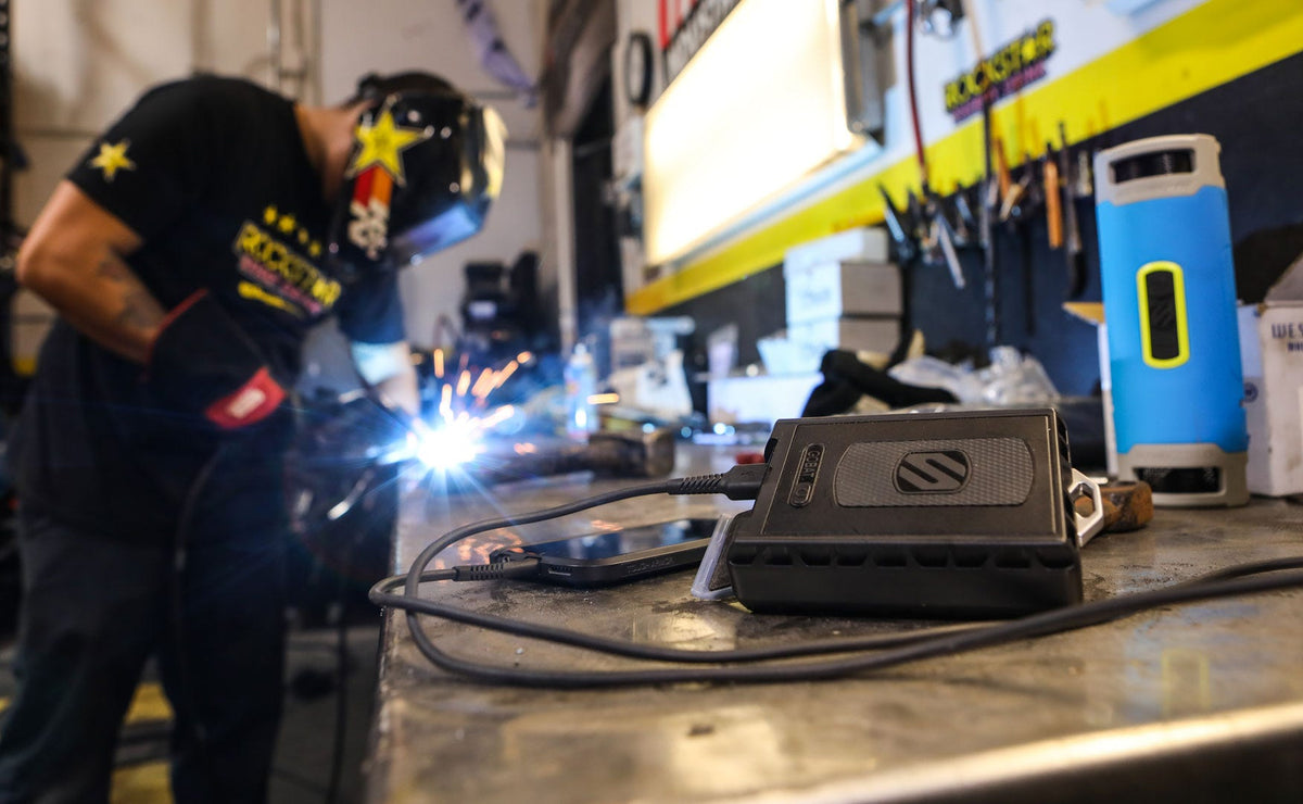 phone charging via power bank in machine shop with man welding in background