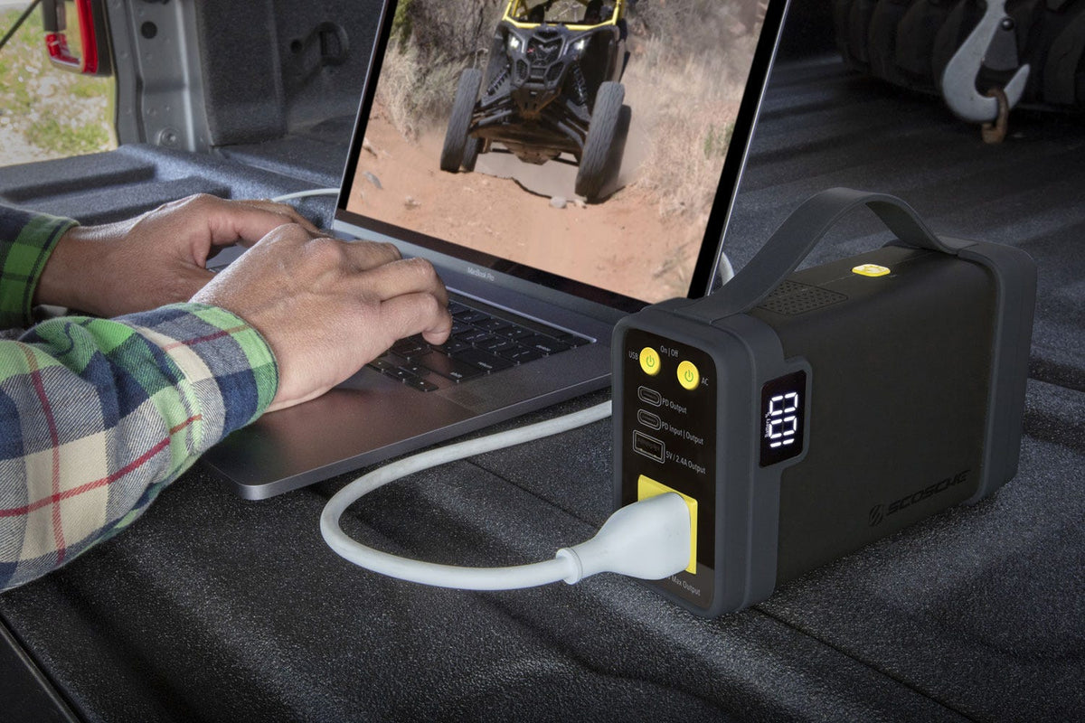 man using laptop on truck tailgate while plugged in to portable power station