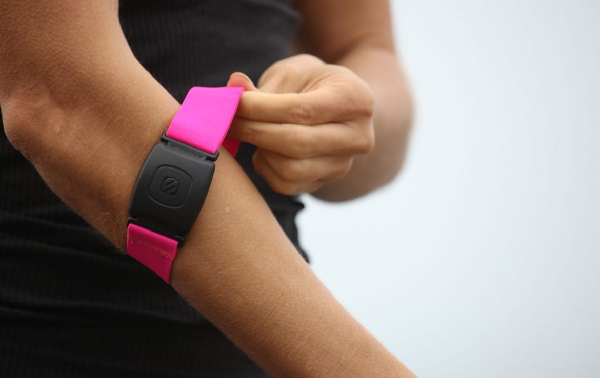 close up of woman grabbing pink Scosche armband heart rate monitor on arm