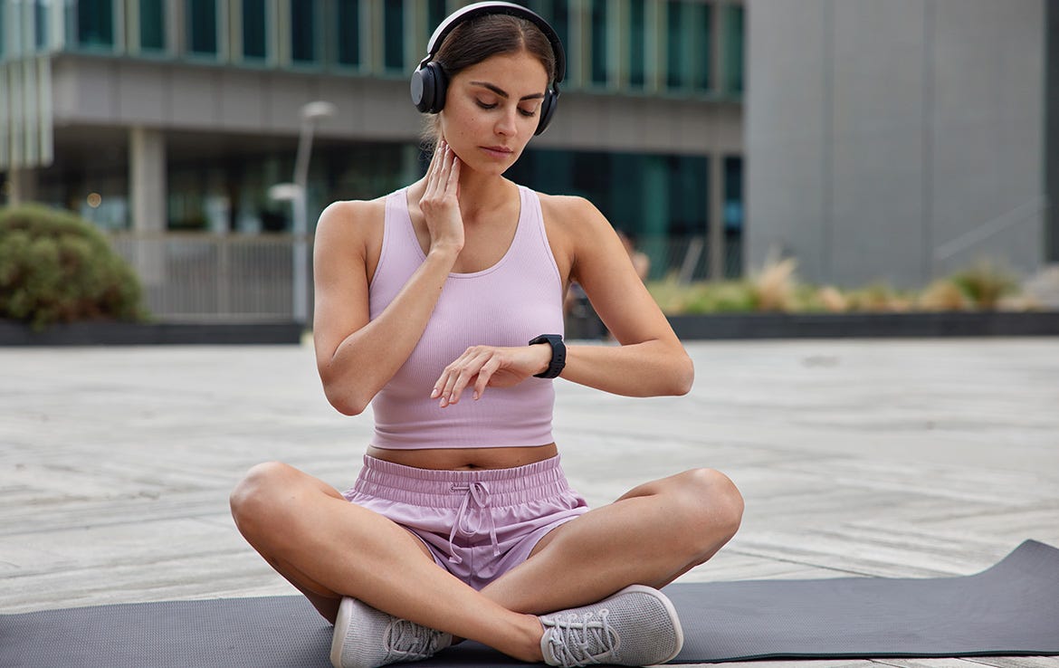 woman sitting on yoga mat checking heart rate while looking at watch