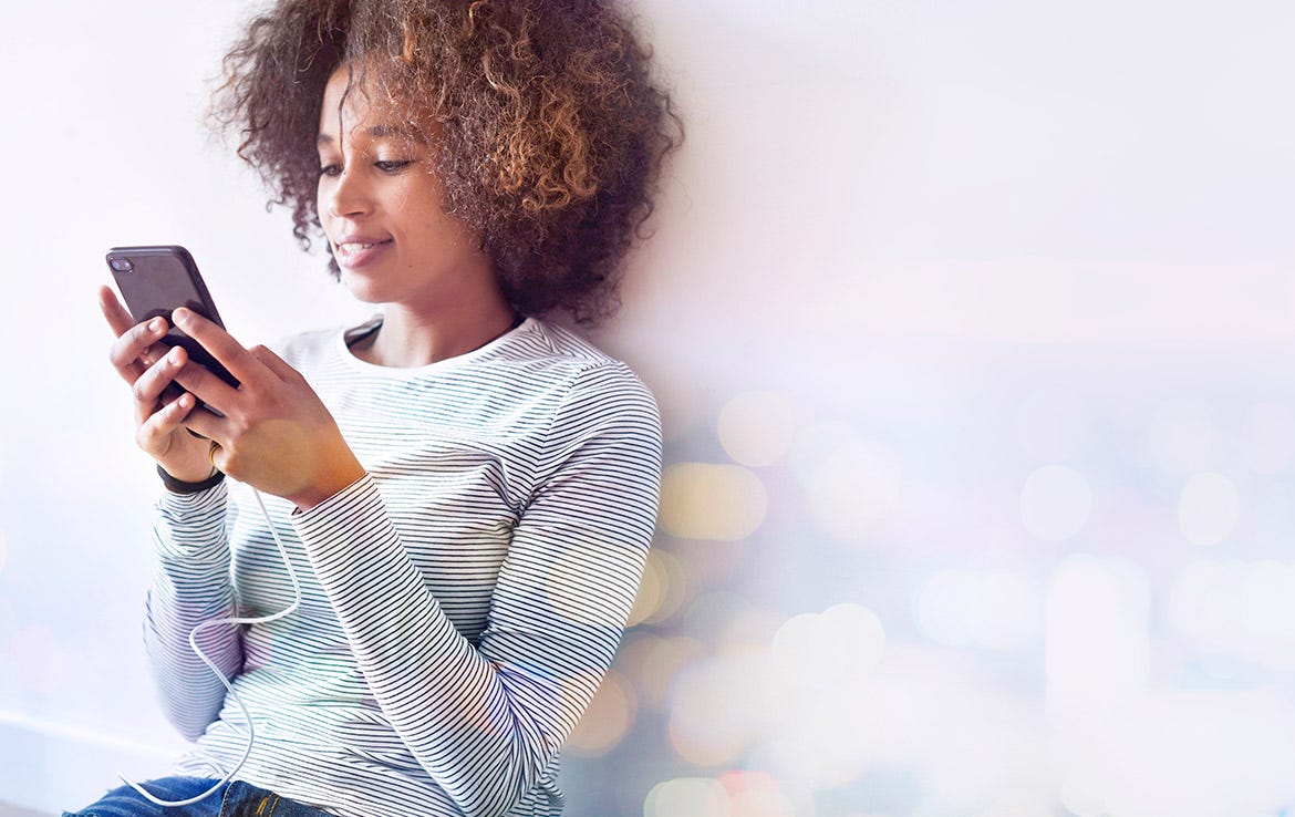 woman holding phone with cable attached while sitting against wall