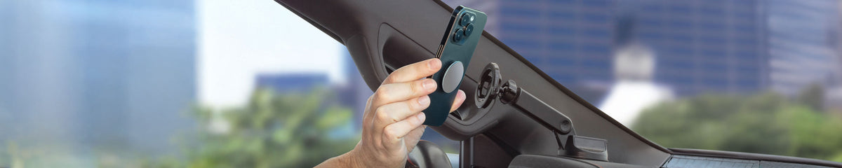 Hand holding a phone up to a phone mount attached to a dashboard of a vehicle