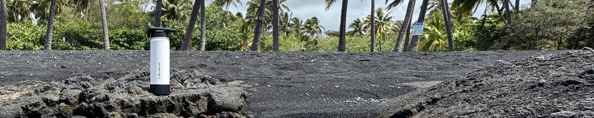 Waterbottle on a rock on a black sand beach with palm trees in the background