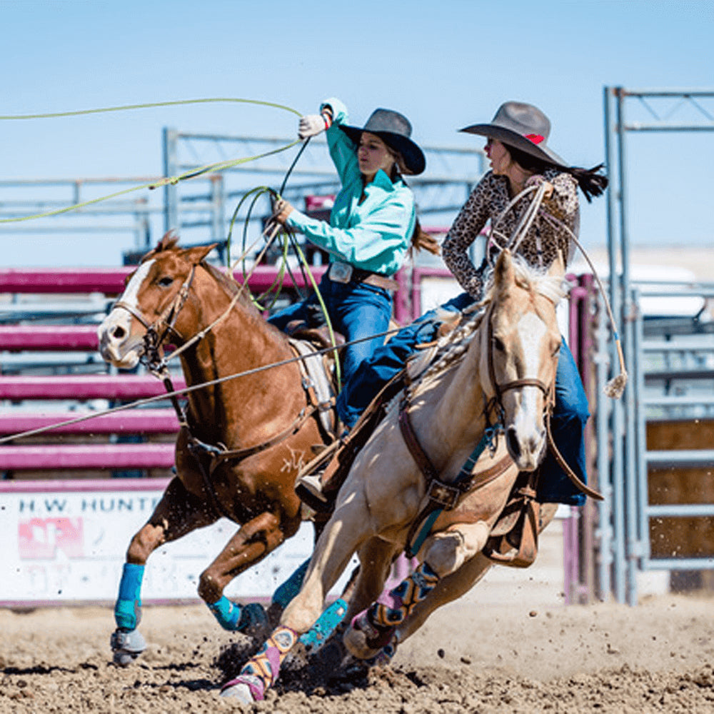Two cowgirls ride their horses in a rodeo. Pfieffer is wearing blue jeans and a leopard print shirt.