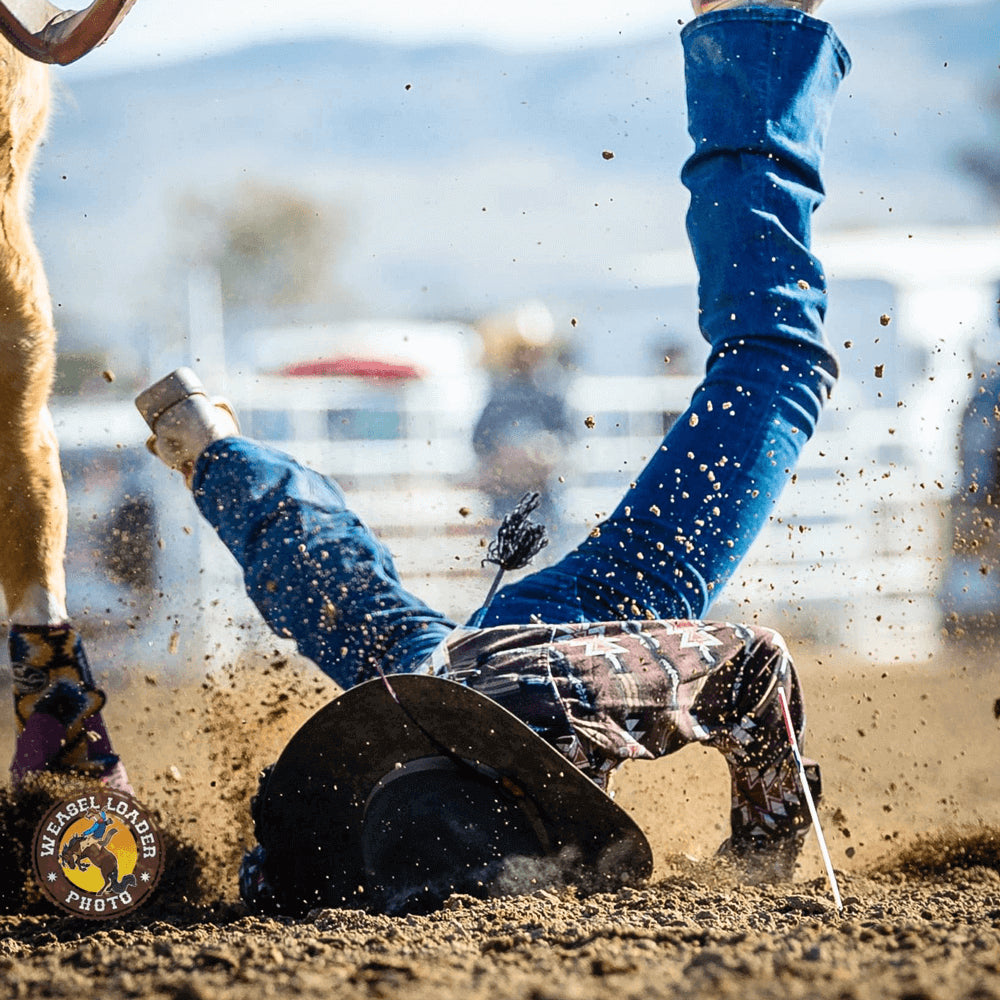 A cowgirl lands face first in the dirt at a rodeo with a horse standing by her and dirt flying up