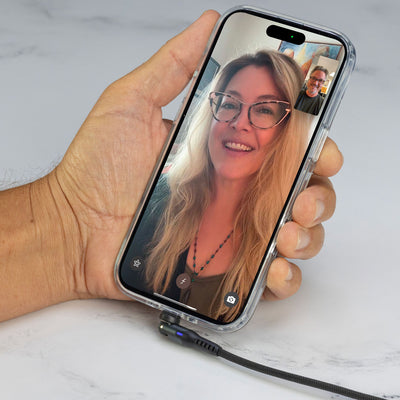 Hand holding phone with FaceTime with woman on screen and a cable plugged into it the bottom of the phone