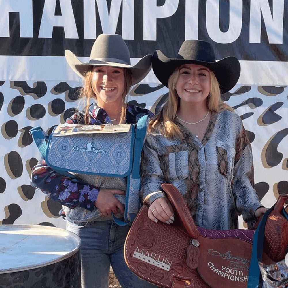 Two cowgirls stand on a rodeo podium holding prizes