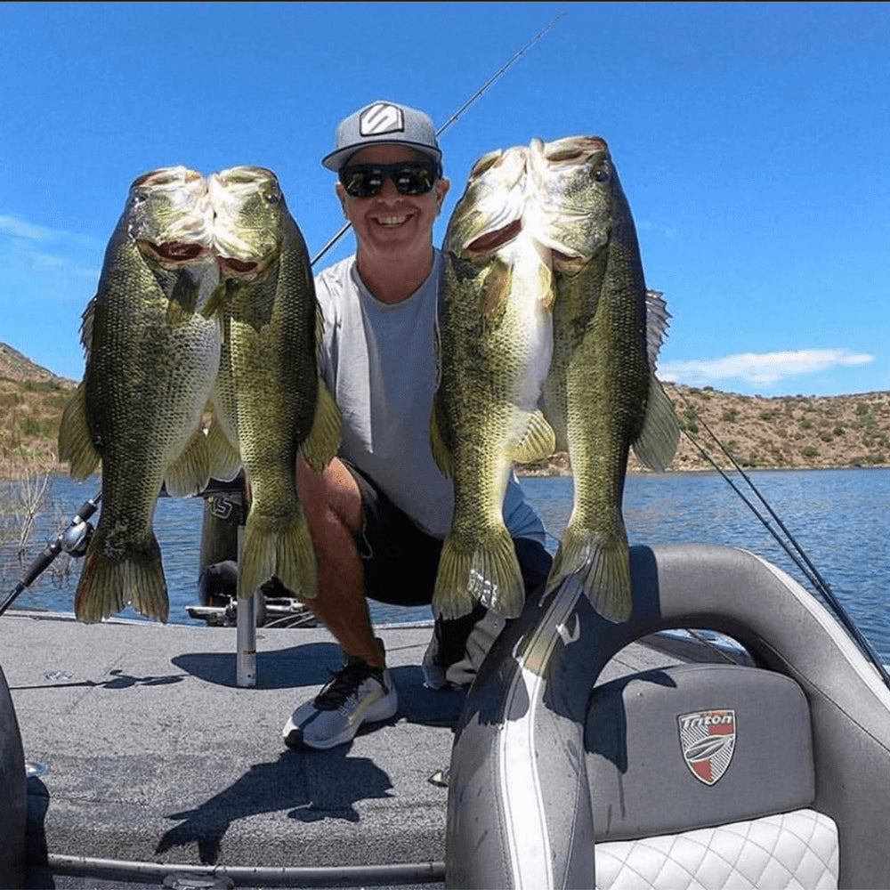 Man kneeling on a boat holding up four fish