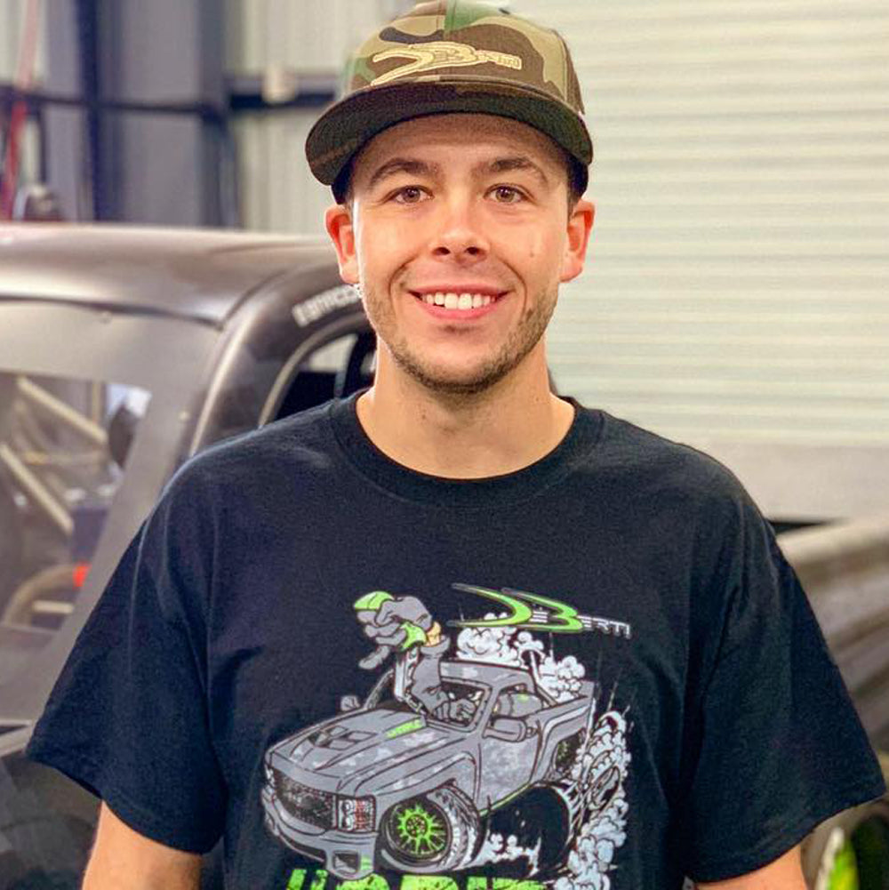 Brad Deberti stands in his garage with a hat and t-shirt on, smiling.