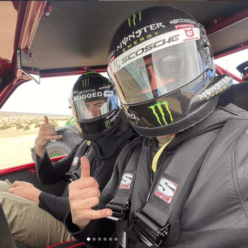 Two men in racing helmets sitting in the cab of a race truck