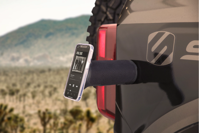 Black BoomBottle magnetically placed on the side of a truck, with an iphone placed on the other end of the speaker